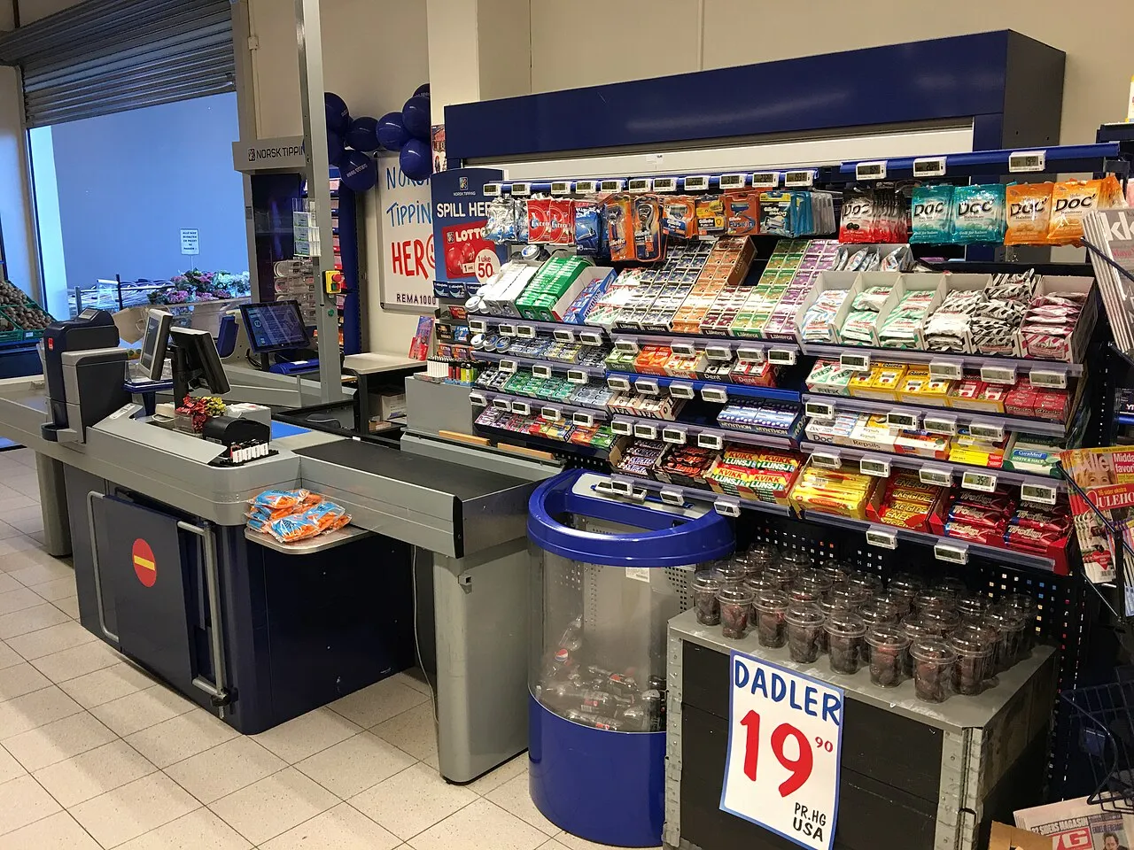 Interieur van een REMA 1000-supermarkt in Tønsberg, Noorwegen, met een kassamedewerker bij de kassa.